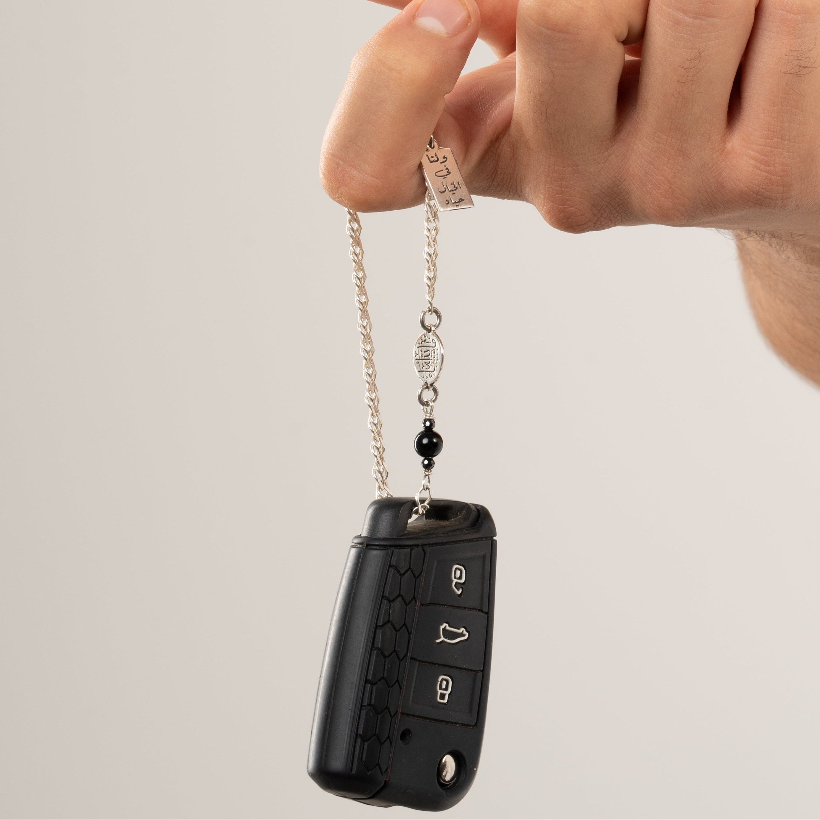 Person holding a car key fob with a keychain against a plain background